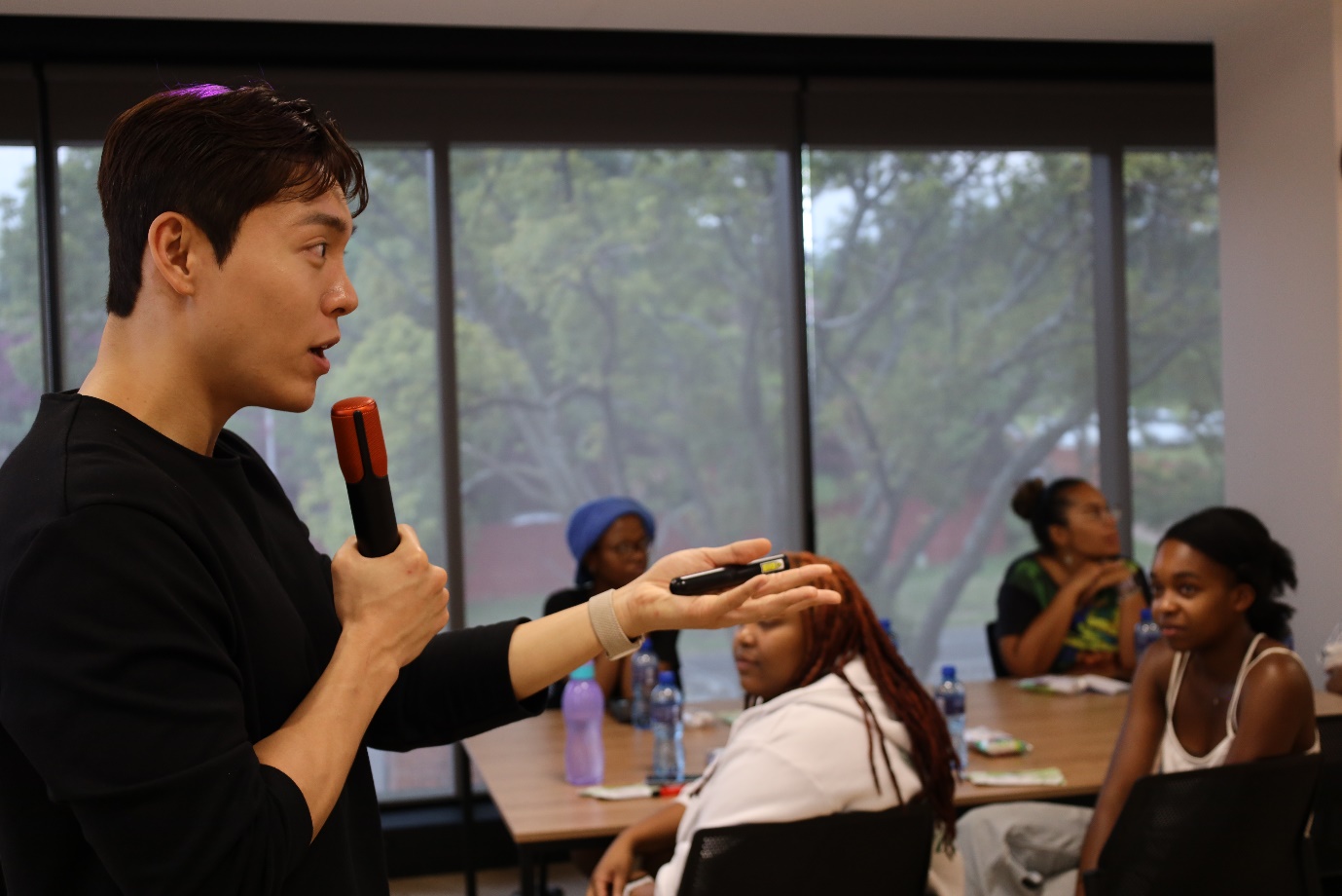 A person holding a microphone in front of a group of people

Description automatically generated