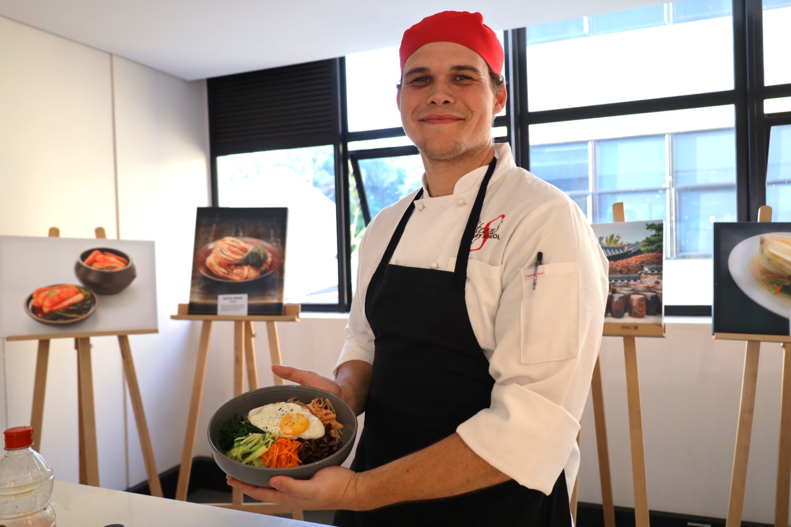 A person in a chef's uniform holding a bowl of food

Description automatically generated