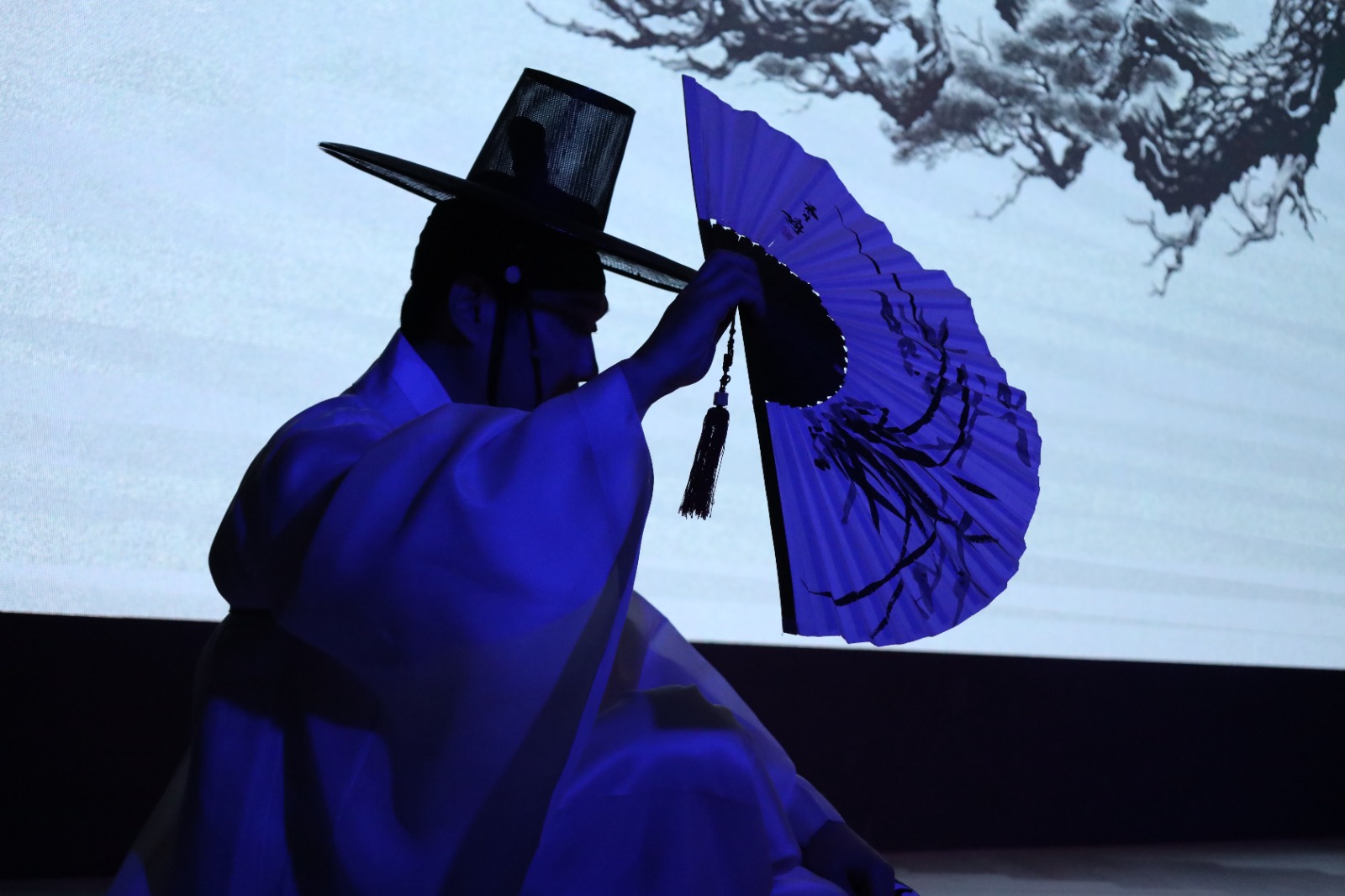 A person wearing a hat and holding a blue fan

Description automatically generated