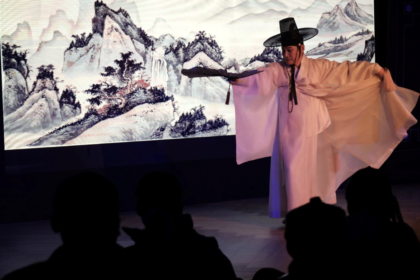 A person in a white robe and hat performing on stage

Description automatically generated