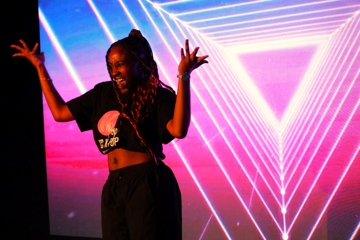 A person with her hands up in front of a pink and purple triangle
Description automatically generated